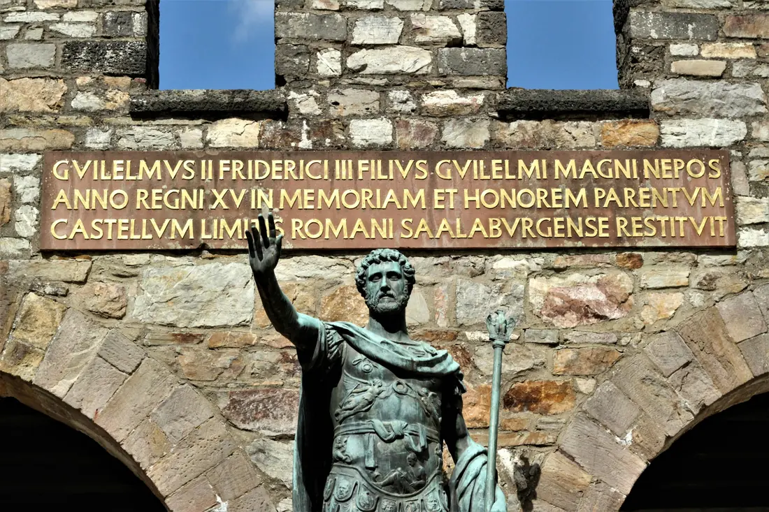 A statue below a stone gate with a Latin inscription